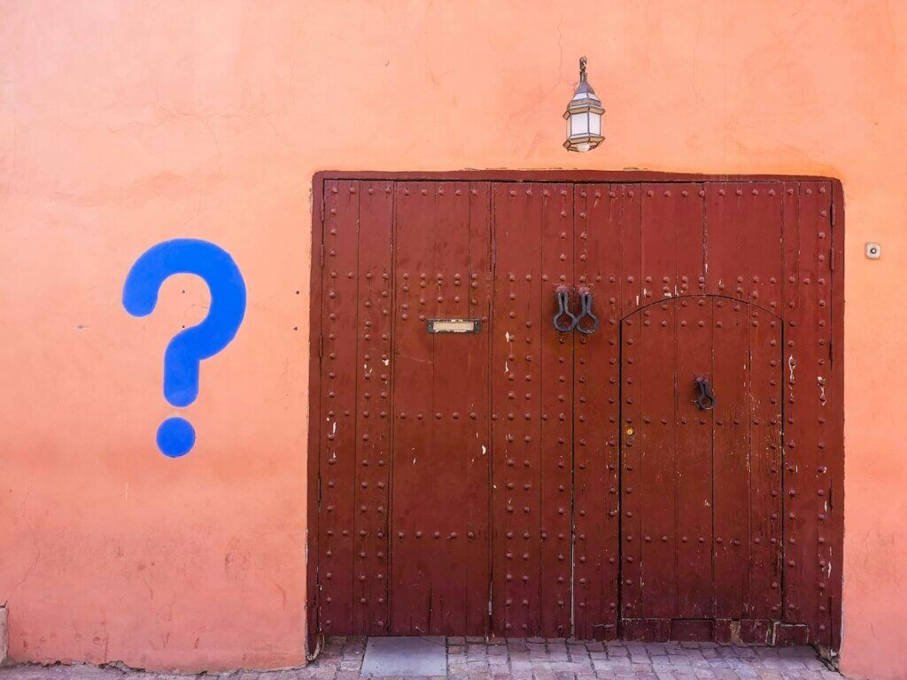 A blue question mark is painted on a pink wall in an alley next to brown metal doors