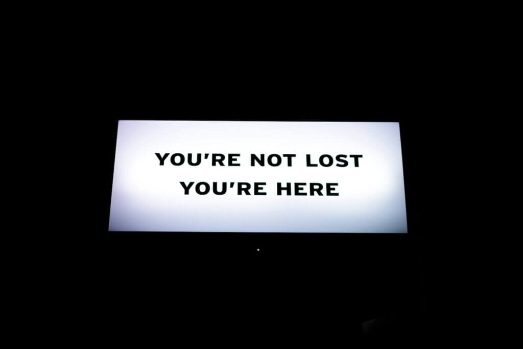White electric sign with black text reads "you're not lost, you're here" representing a feeling lost career phase and the mindset of moving through it
