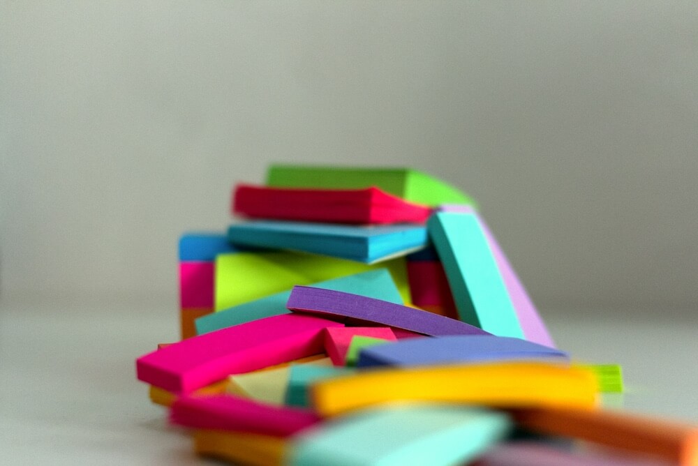 a large pile of multi-colored sticky note pads stacked on a grey table in a grey studio background setup.